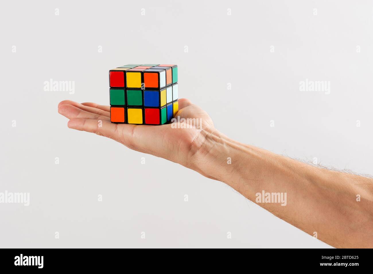 Uomo che tiene un puzzle Rubiks Cube irrisolto sul palmo della mano si estendeva su uno sfondo bianco Foto Stock