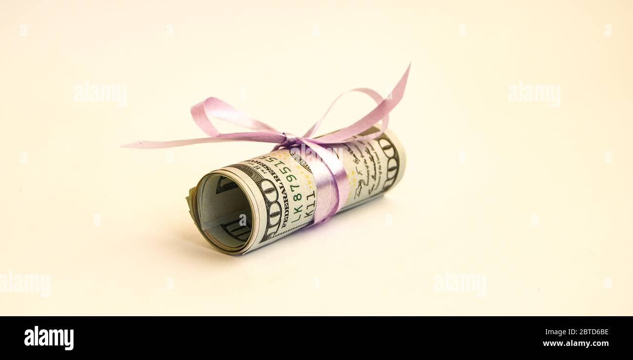Piccolo dono del dollaro, pacchetto di fatture di cento dollari legati con un nastro rosa. Dollari isolati su sfondo bianco Foto Stock