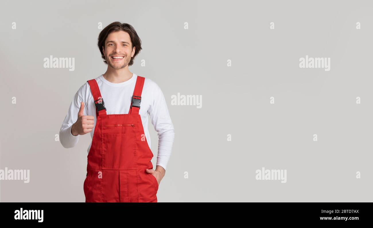 Concetto di Handyman Services. Smiling Young Workman in uniforme con il pollice in alto Foto Stock