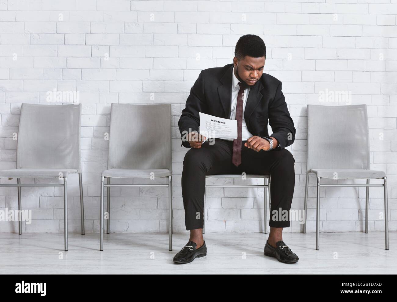 Uomo d'affari nero serio con il resume che aspetta l'intrview di lavoro, guardando il suo orologio da polso nella lobby dell'azienda. Spazio vuoto Foto Stock
