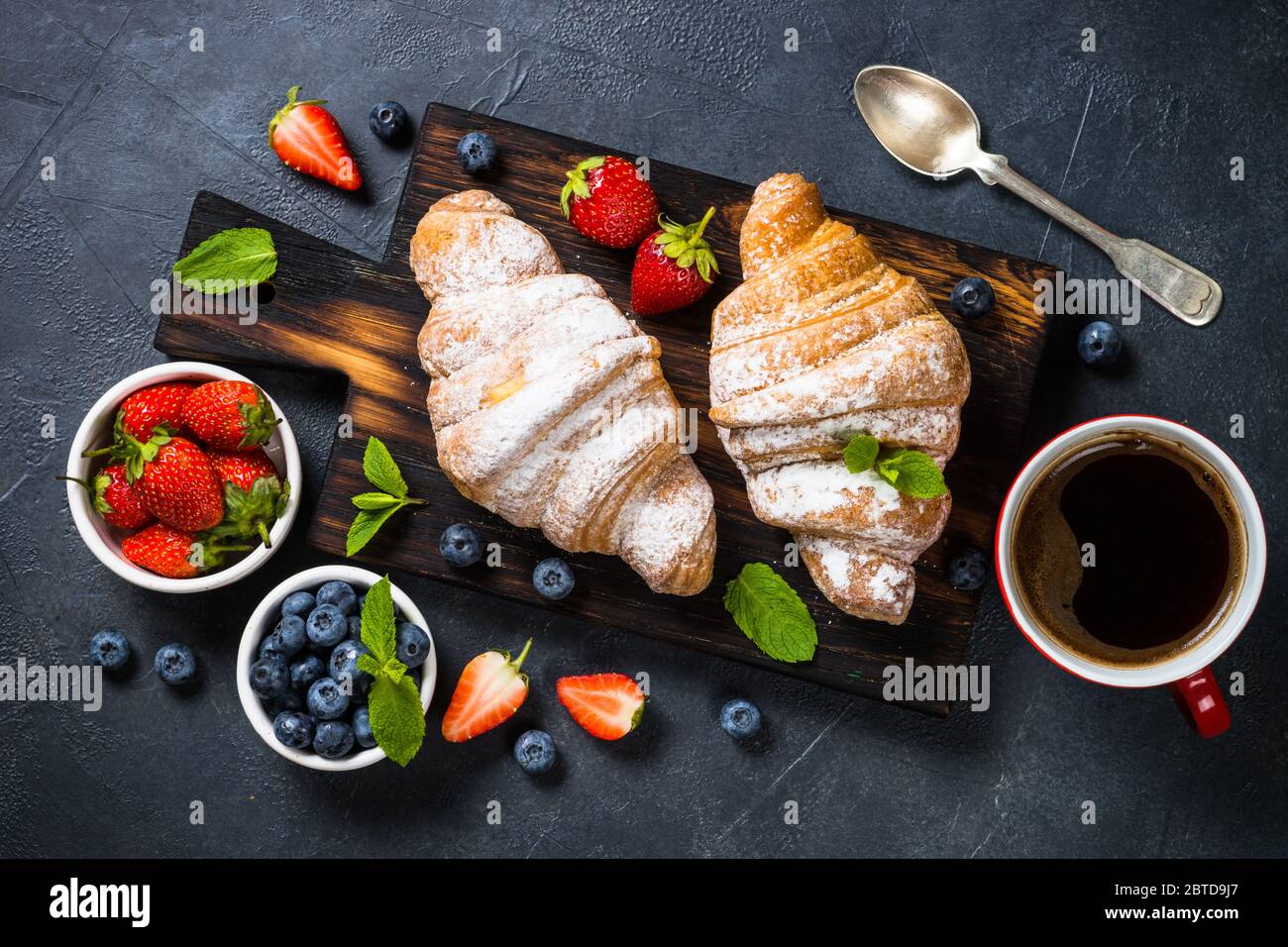 Croissant con frutti di bosco freschi e la tazza di caffè nero. Foto Stock