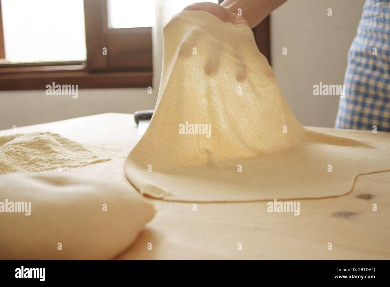 Preparazione della pasta fresca fatta in casa: La mano della donna retroilluminata mostra la trasparenza della pasta fresca appena srotolata, la pasta tradizionale italiana, la donna cucina t Foto Stock
