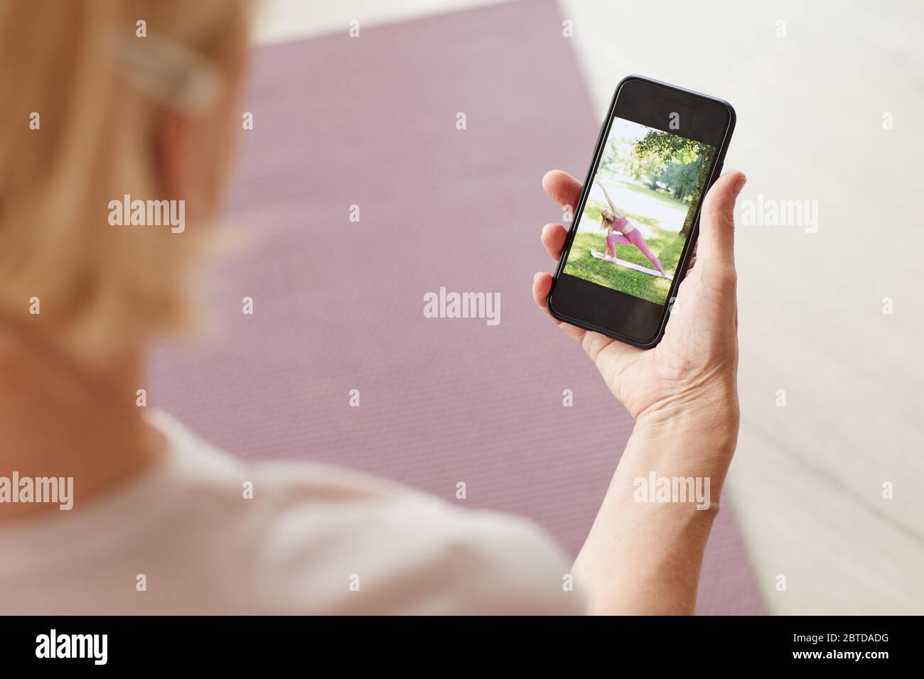Donna che tiene il telefono cellulare in mano e che guarda lo yoga online a casa Foto Stock