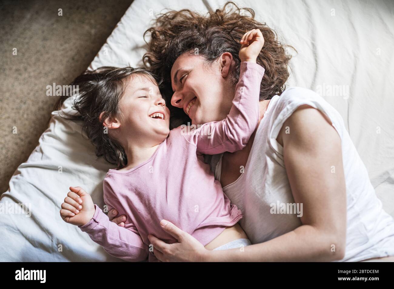 Una madre e sua figlia sorridono mentre si carezzano e giocano intorno su un letto Foto Stock