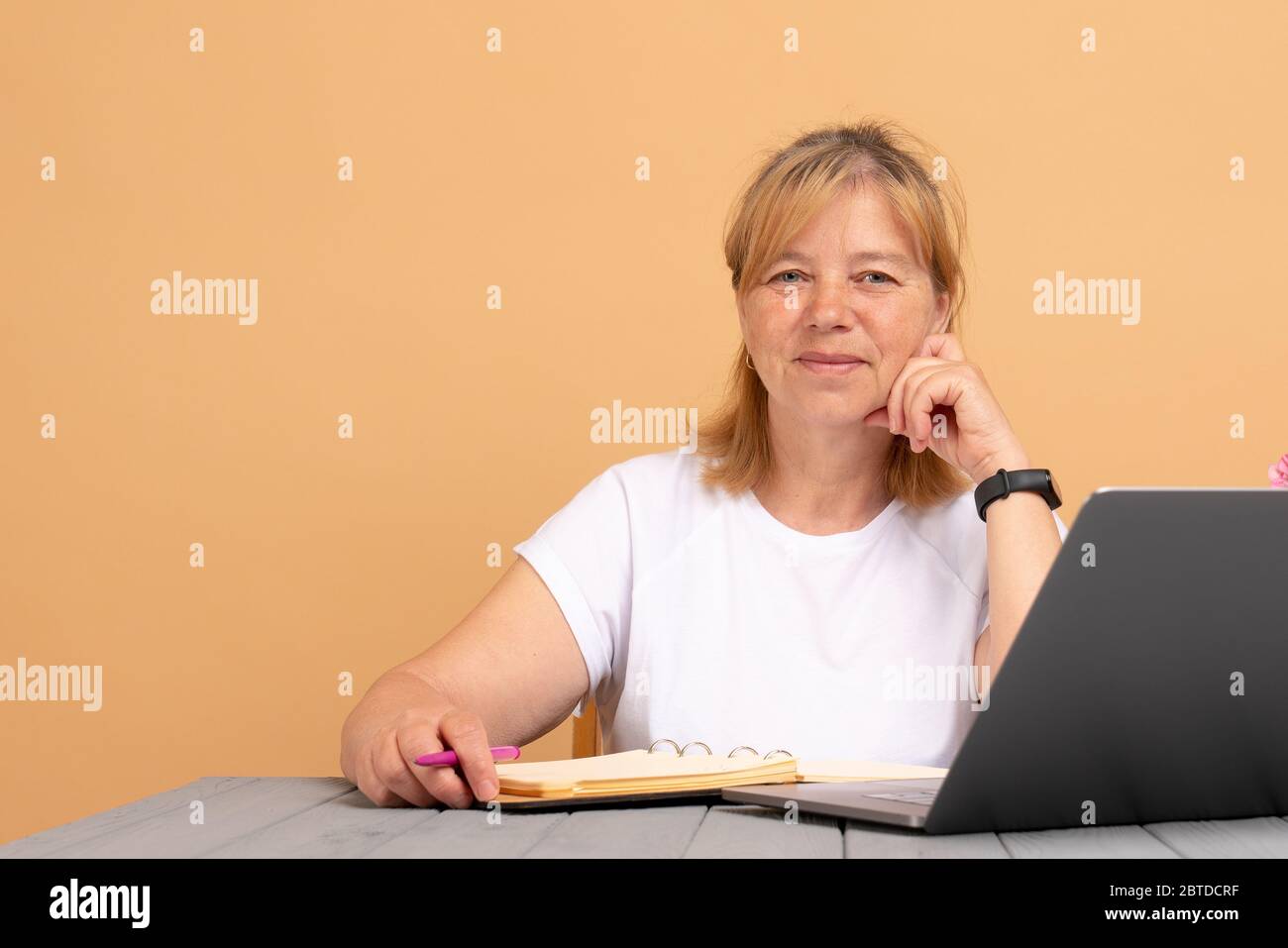 Attraente positivo donna matura di talento scrittore seduto di fronte al portatile e la scrittura del suo nuovo libro, guardando la fotocamera con joyfull sorriso Foto Stock