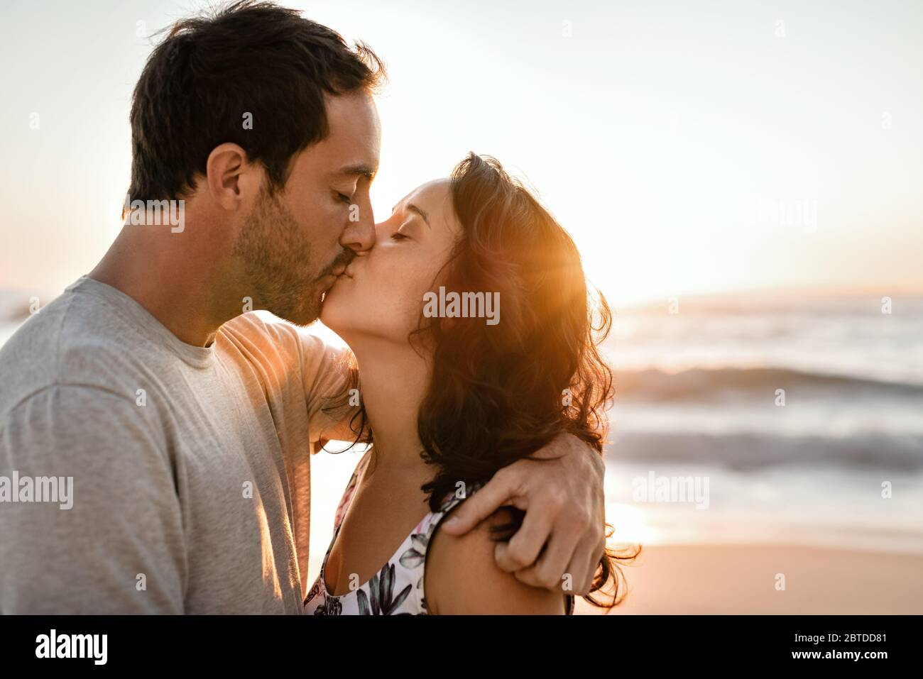 Una giovane coppia che ama baciarsi su una spiaggia al tramonto Foto Stock