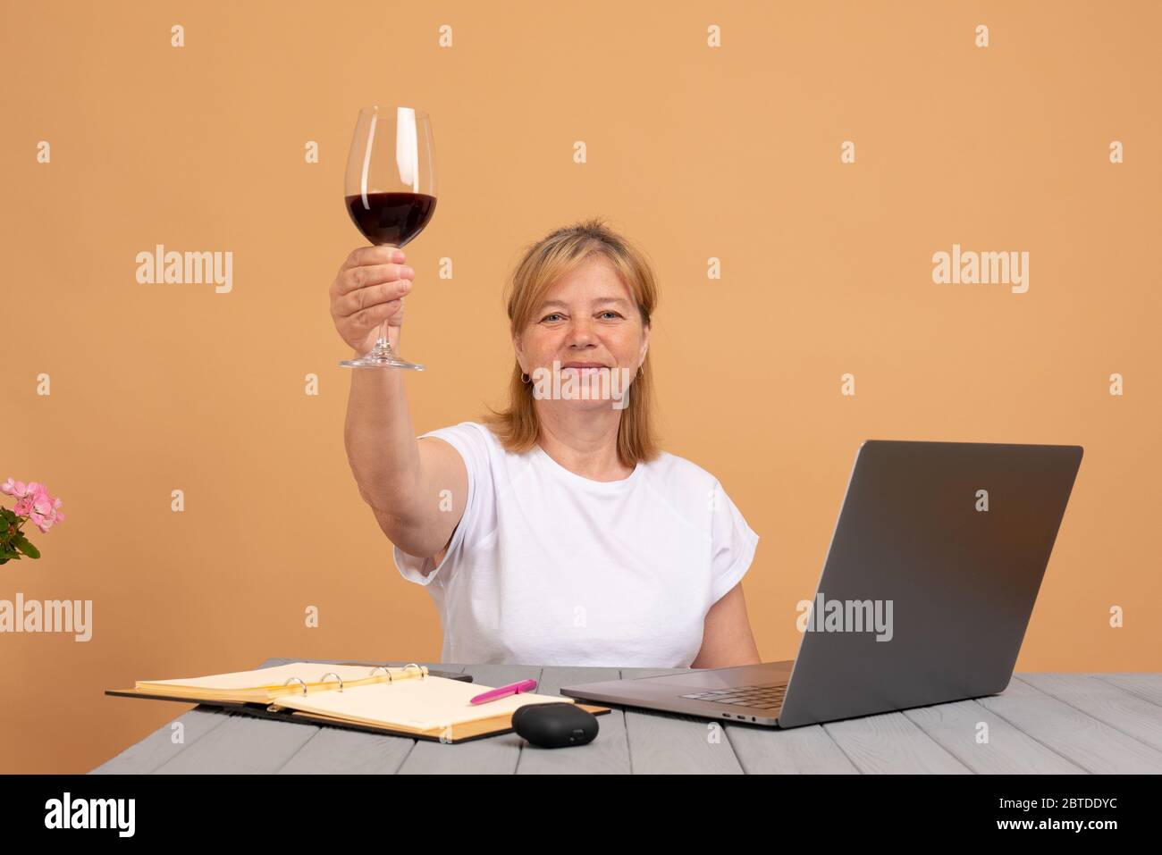 Felice donna matura che usa il computer portatile e bere vino, mostra il segno di auguri Foto Stock