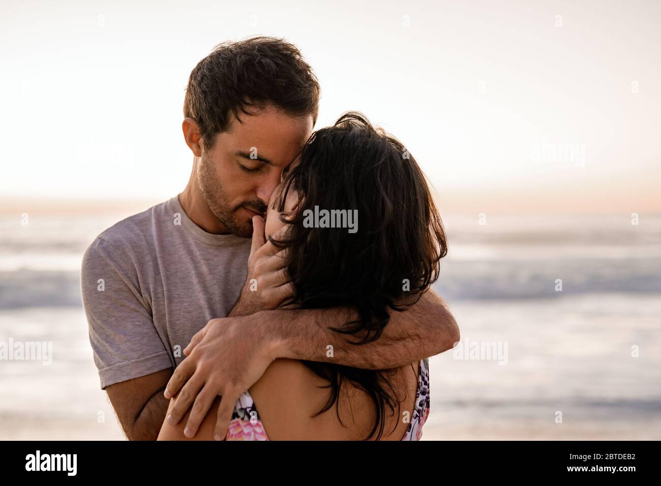 Coppia che condivide un romantico abbraccio su una spiaggia al tramonto Foto Stock