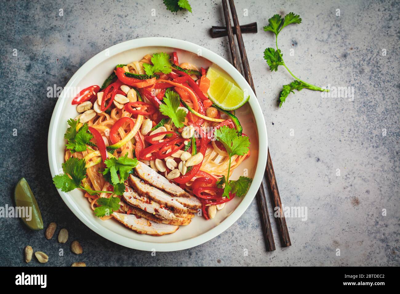 In un recipiente, a sfondo scuro, si imbottiggano noodle thailandesi con pollo, arachidi e verdure. Foto Stock