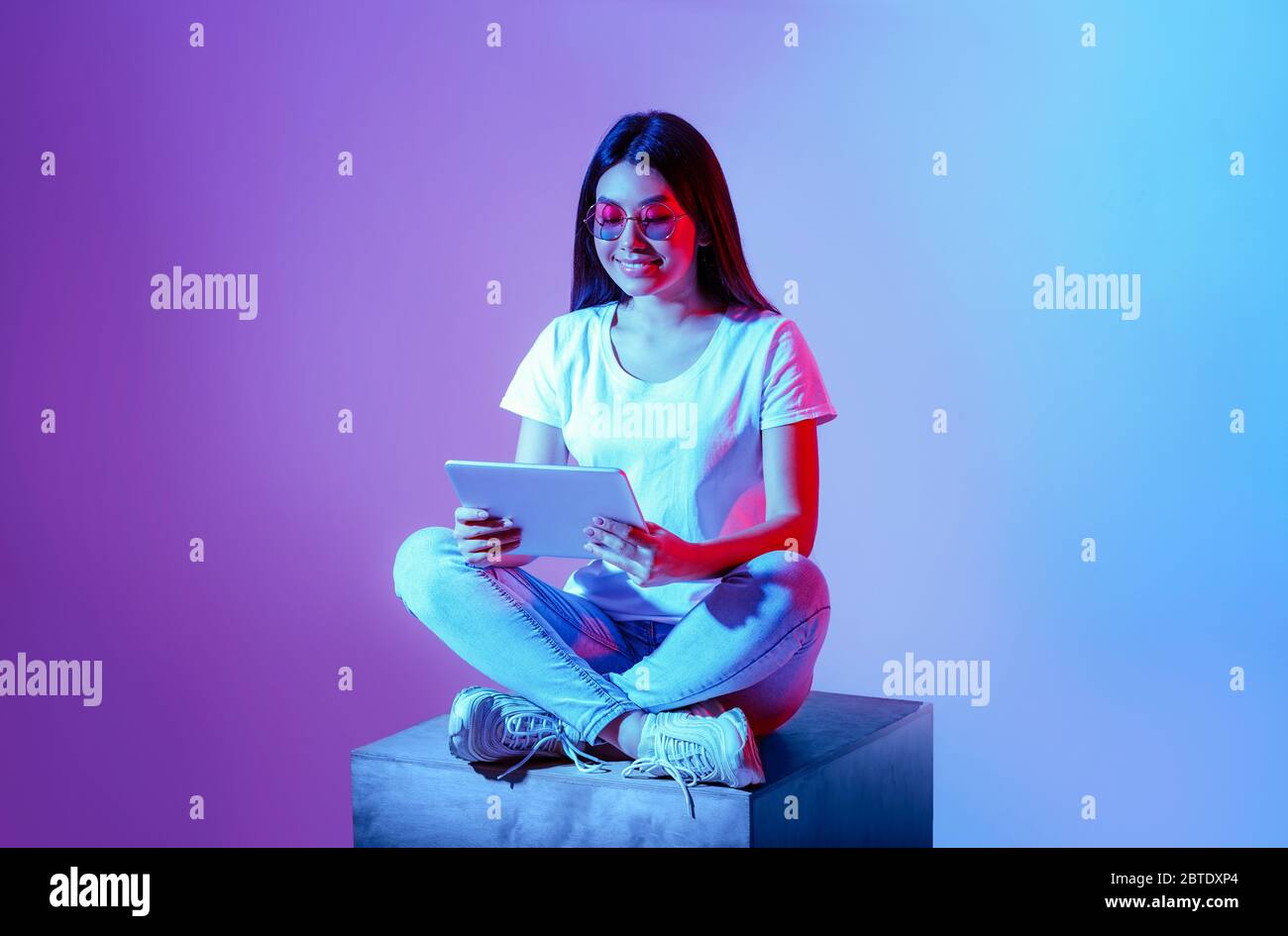 Nuova generazione. Millennial ragazza in occhiali rotondi si siede con le gambe ripiegate con la tavoletta Foto Stock