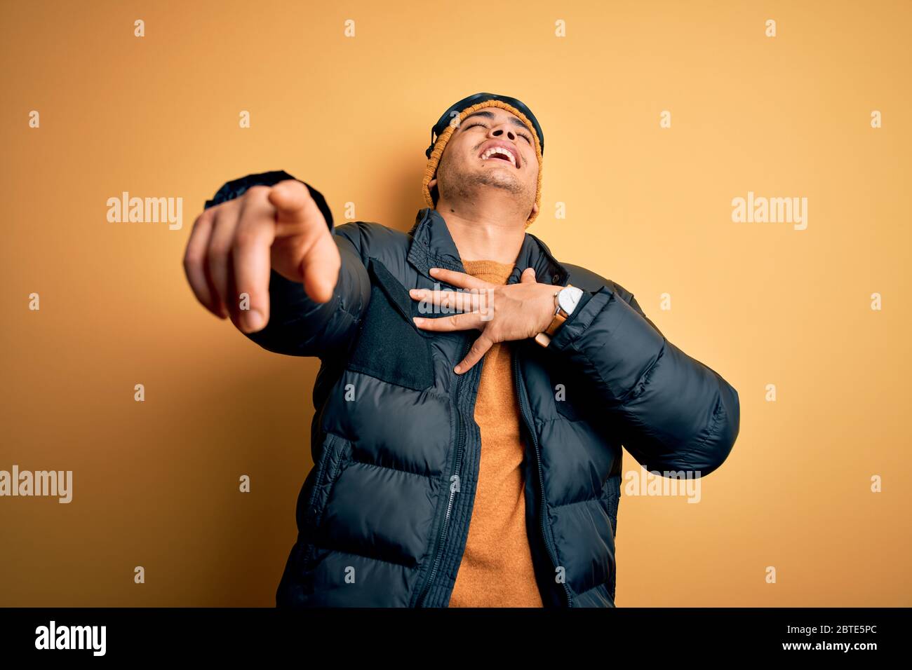 Giovane sciatore brasiliano uomo che indossa abbigliamento sportivo da neve  e occhiali da sci su sfondo giallo sorridente con lingua fuori mostrando le  dita di entrambe le mani facendo v Foto stock 