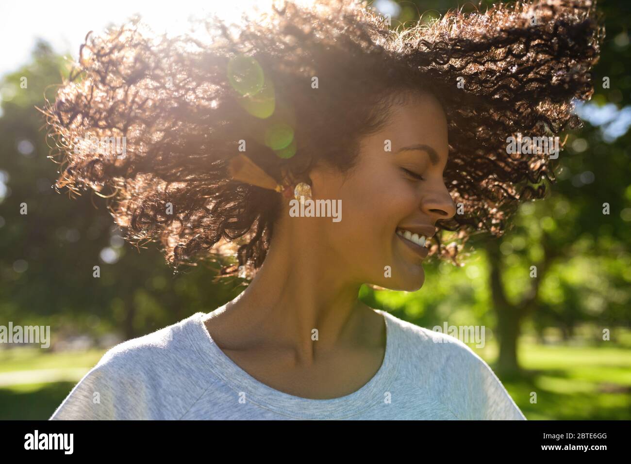 Donna ridente che tondolava i capelli ricci all'esterno in un parco Foto Stock