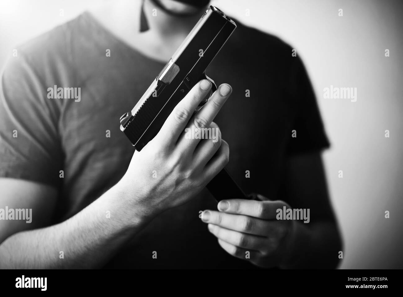 Immagine in bianco e nero di un uomo in una t-shirt che tiene una pistola e la sostituisce con una rivista con cartucce. Pericolo. Esercito. Killer. Foto Stock