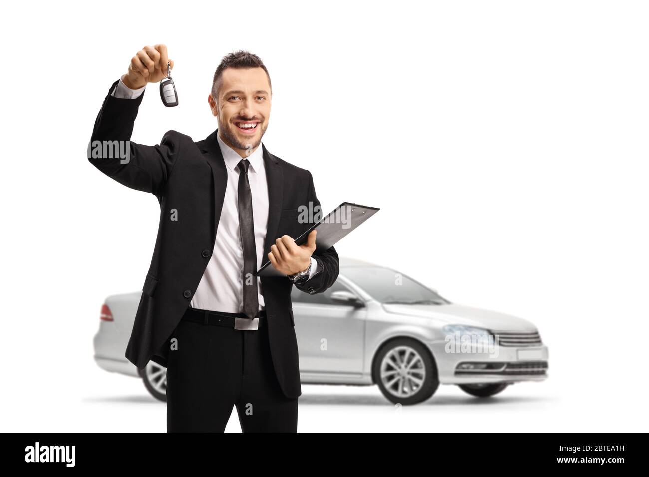 Uomo in tuta con chiave auto e posa davanti a una nuovissima auto color argento isolata su sfondo bianco Foto Stock