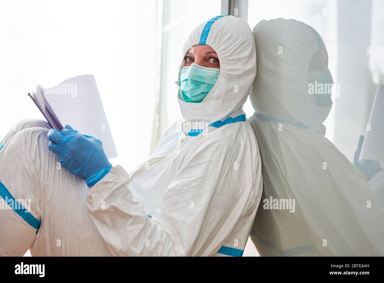 Il dipendente del reparto sanitario in abbigliamento protettivo contiene una lista di controllo per il monitoraggio dei contatti durante la pandemia di Covid-19 Foto Stock