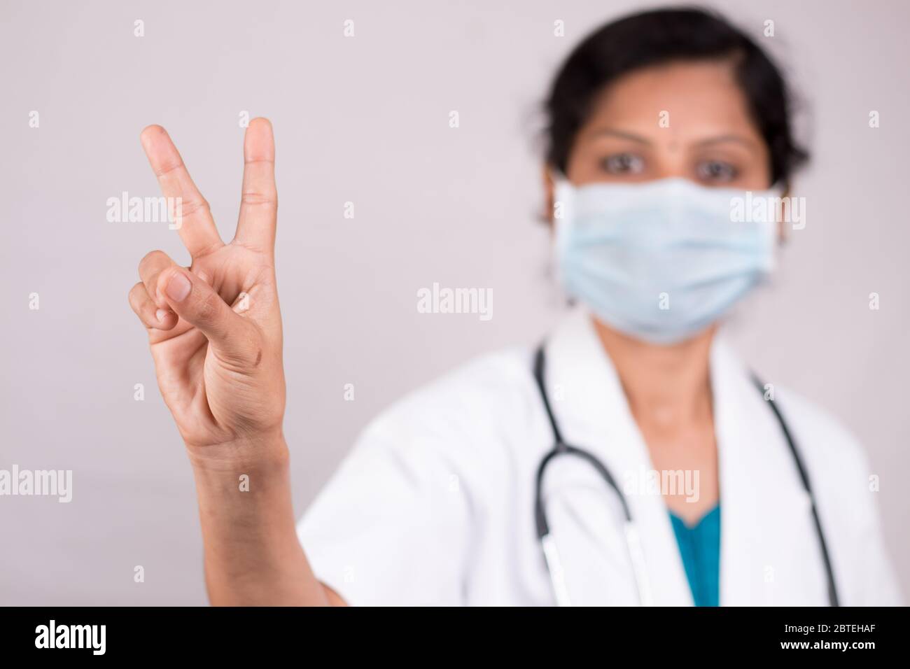 Donna medico con maschera medica in uniforme mostrando V gesto su sfondo isolato - concetto di vittoria saluto o gesto di pace da parte del medico durante il covid Foto Stock