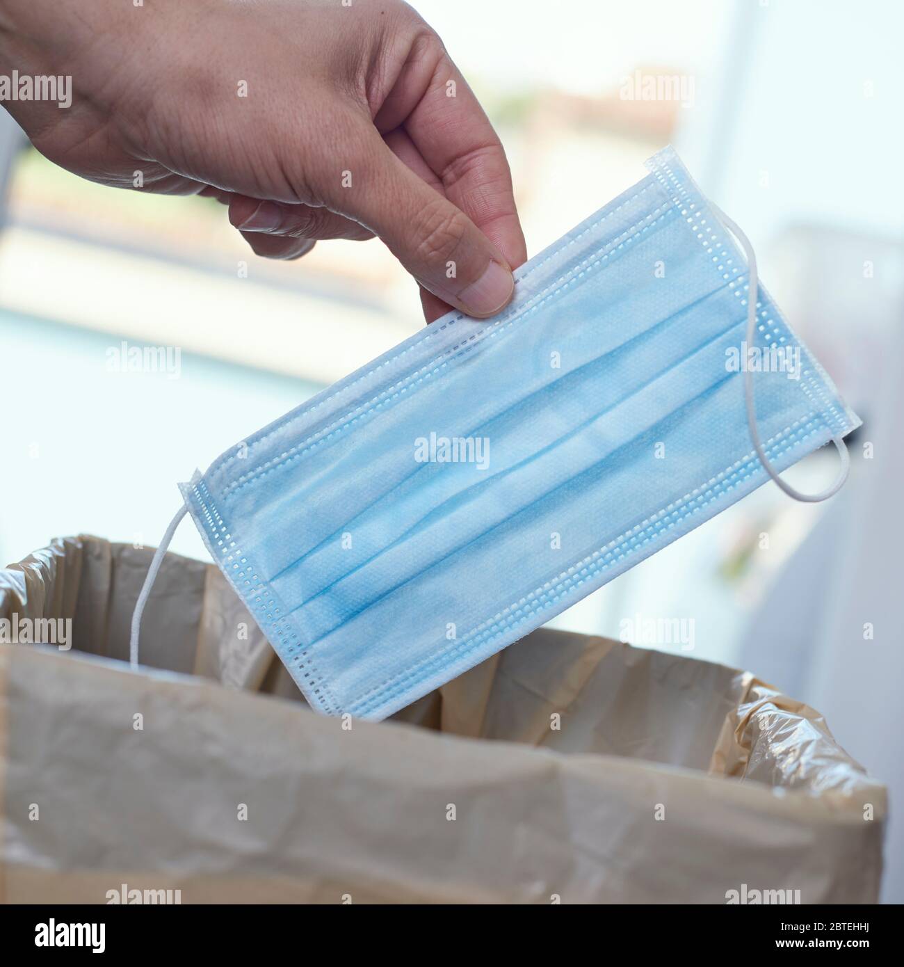 primo piano di un uomo che lancia una maschera chirurgica al cestino può Foto Stock