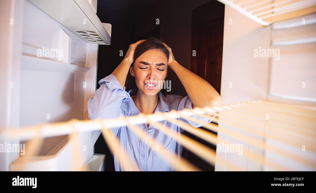 Disperata casalinga in disperazione guardando un frigorifero vuoto Foto Stock