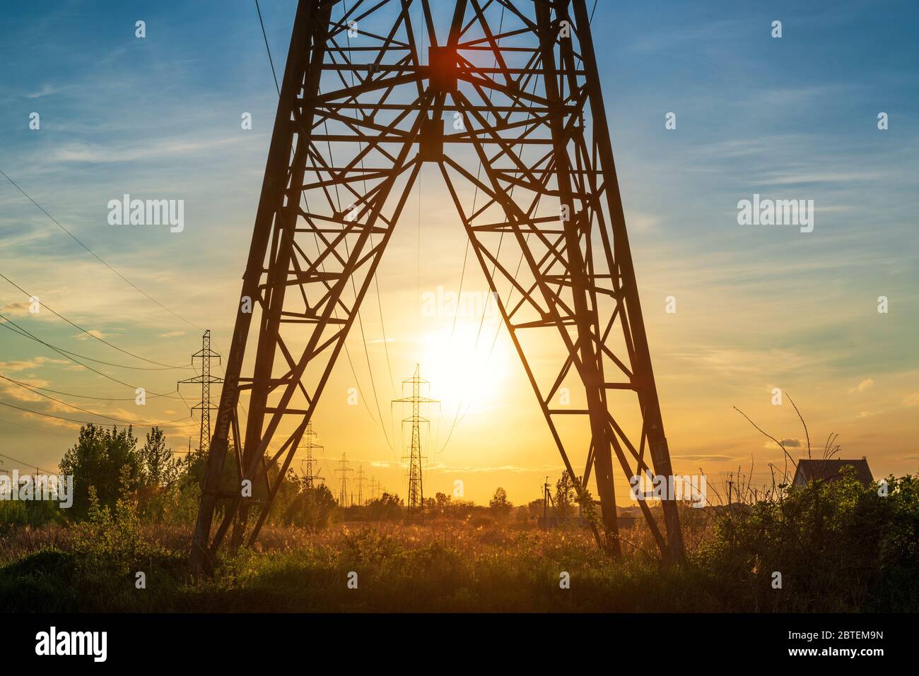 La linea elettrica supporta la torre e il sole del tramonto. Paesaggio industriale Foto Stock