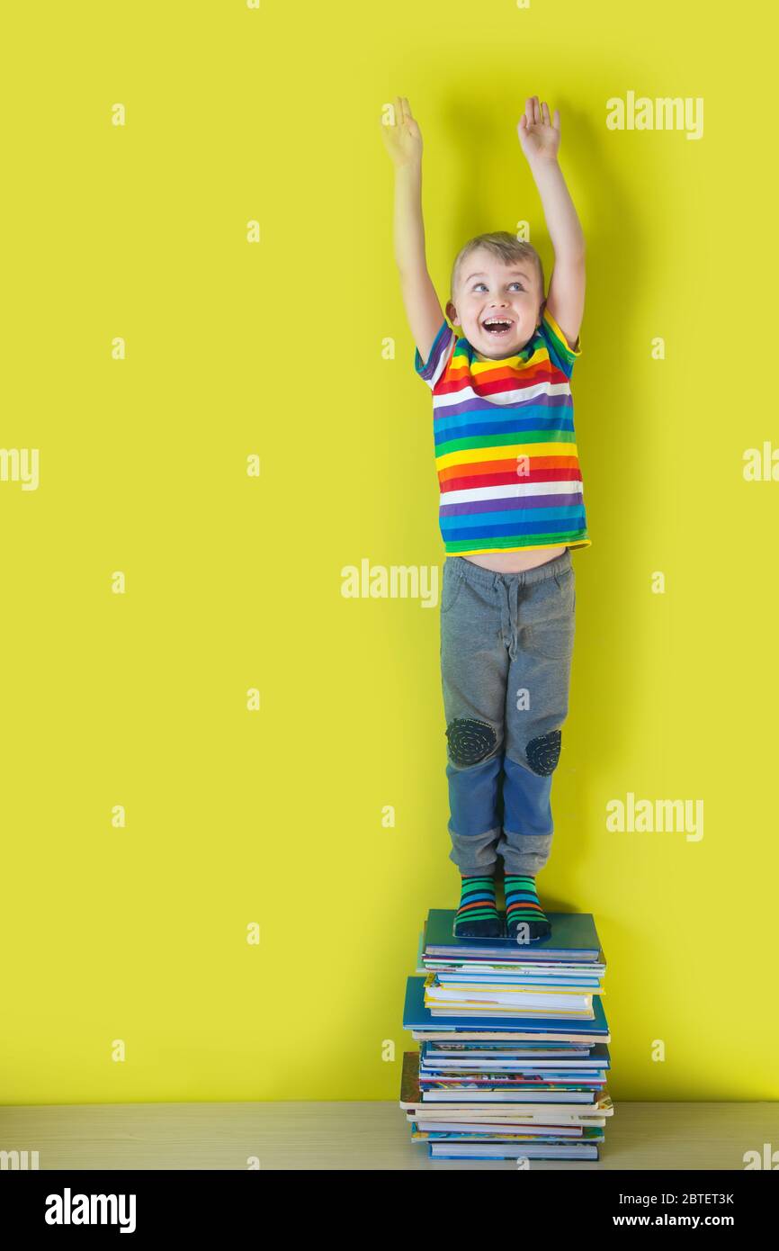 Un bambino sorridente gioioso sta in piedi su una pila di libri per bambini. Sfondo verde. Foto Stock