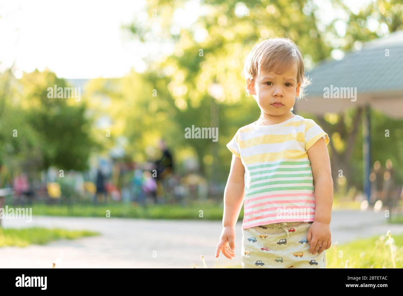 Infanzia, natura, estate, parchi e outdoor concetto - ritratto di carino ragazzo dai capelli biondi in T-shirt multicolore a righe con serosa, triste Foto Stock