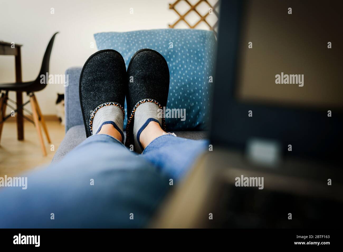 Sdraiati sul divano nelle pantofole con un computer portatile che lavora da casa. Cat sullo sfondo Foto Stock