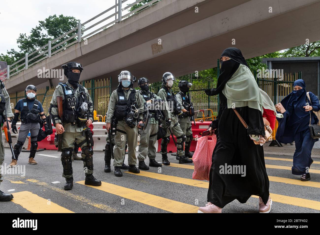 Una donna passa davanti a poliziotti in piedi in guardia nel mezzo della zona di Causeway Bay durante la protesta. Violenza, Arresti e uso di cannoni ad acqua tornarono nelle strade di Hong Kong con centinaia di manifestanti che marciavano sull'isola di Hong Kong contro i piani della Cina di imporre una legge nazionale sulla sicurezza. Foto Stock