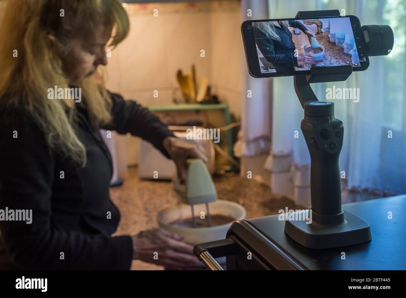 Donna adulta che si filma preparando l'impasto con un mixer per una torta durante la quarantena. Foto Stock