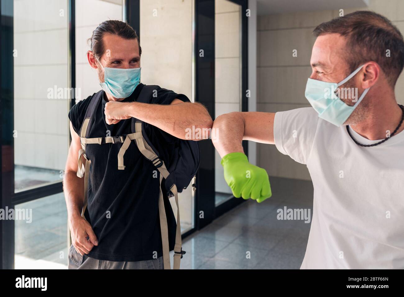 Concetto: Coronavirus, covid-19. Due amici maschi si salutano con i loro gomiti all'ingresso di un edificio. Nuova normalità, pandemie ed epi Foto Stock