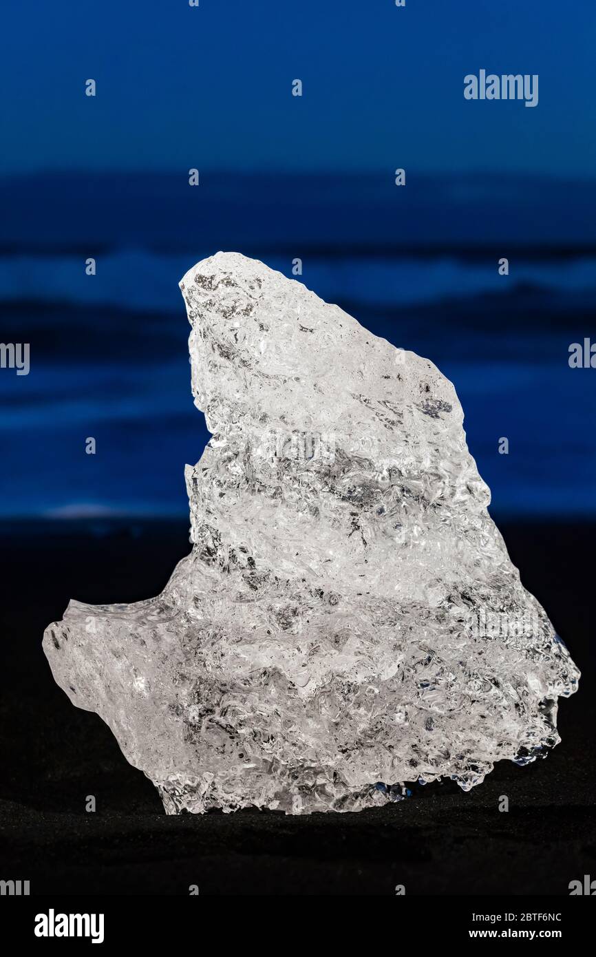 Sciogliendo un pezzo di ghiaccio glaciale limpido, originariamente calato nella laguna di Jökulsárlón dal ghiacciaio Breiðamerkurjökull, a Diamond Beach sulla costa meridionale Foto Stock