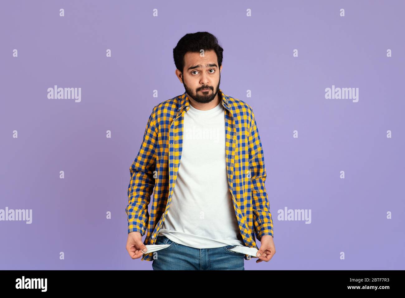 Fallimento e disoccupazione. Uomo indiano sconvolto che mostra tasche vuote su sfondo lilla Foto Stock