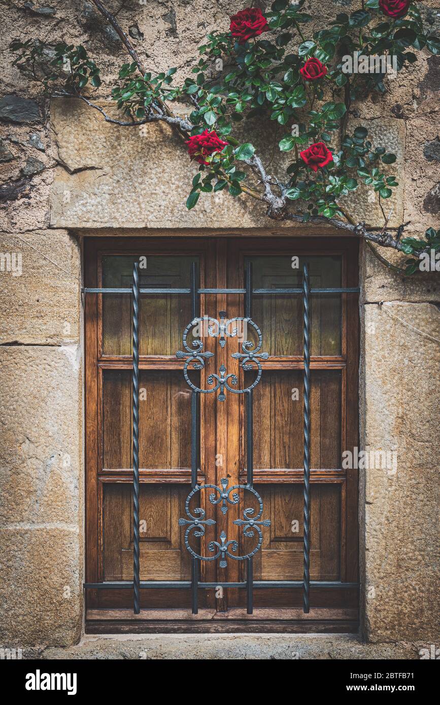 Facciata di una casa tradizionale mediterranea con una finestra in legno a graticcio e rose rosse Foto Stock