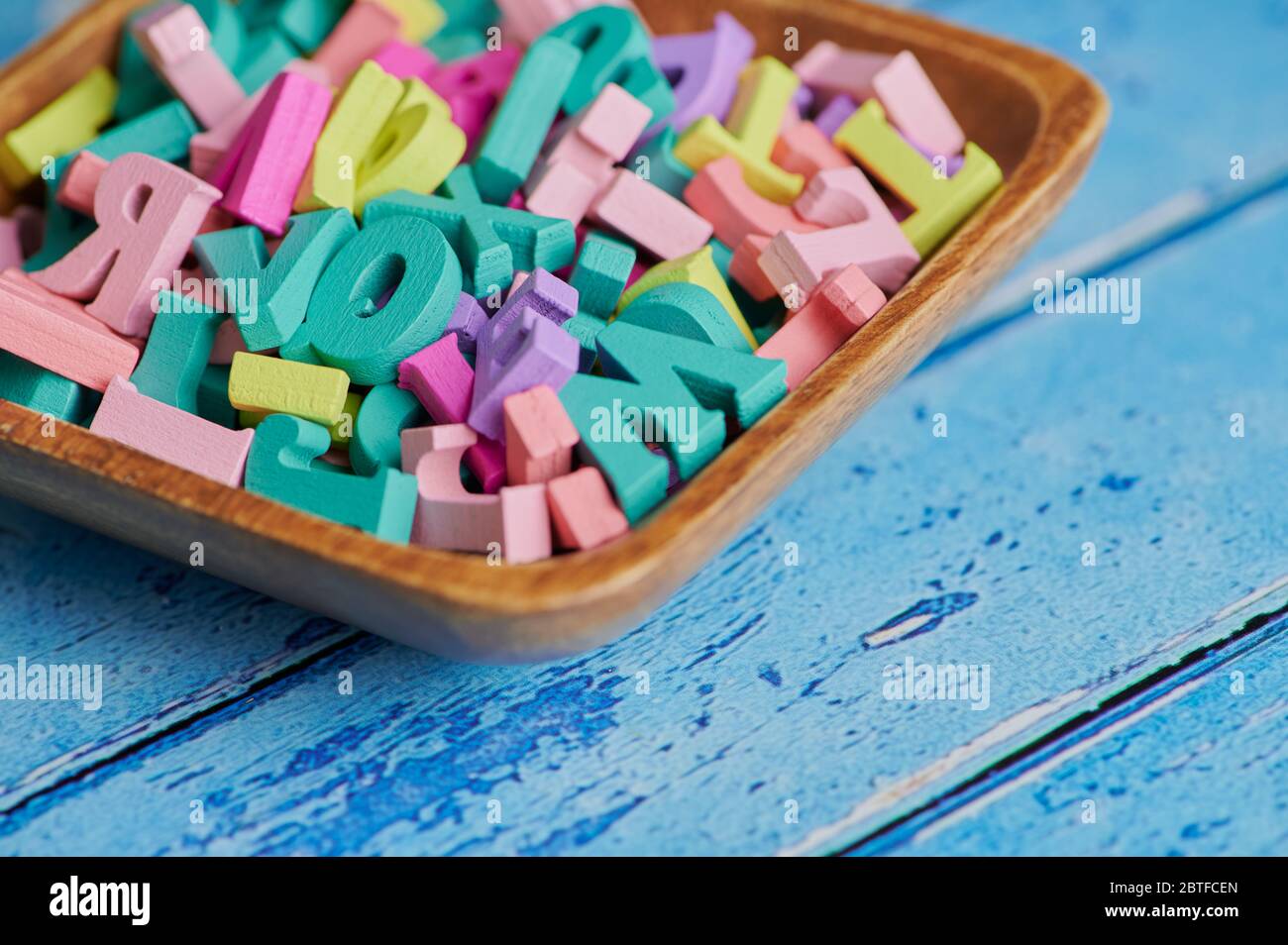 lettere colorate in legno in una ciotola su sfondo blu con spazio per la copia Foto Stock