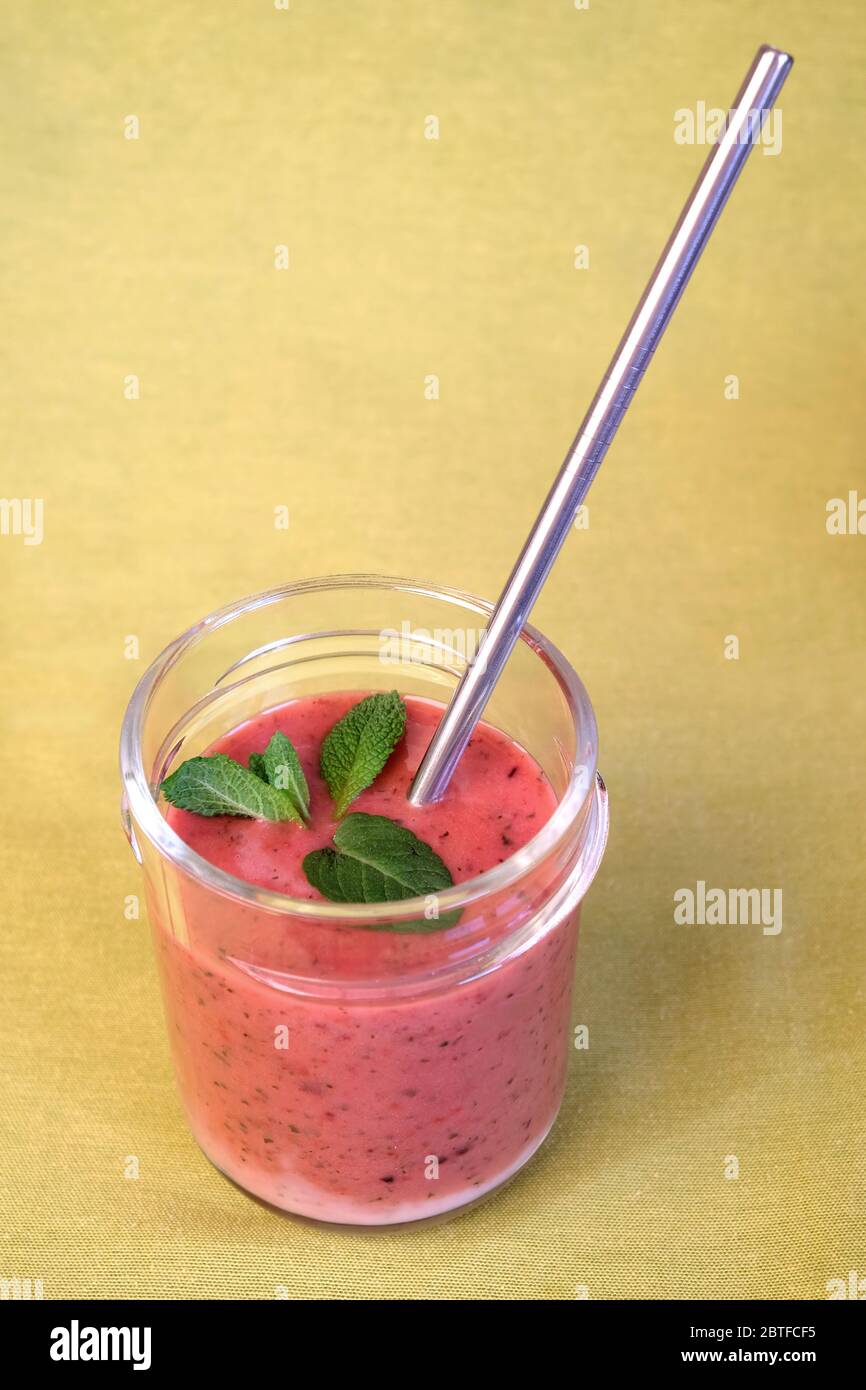 Cocktail frullati di frutta non alcolica con fragola e mora in yogurt con foglie di menta nei bicchieri trasparenti di vino su fondo verde Foto Stock