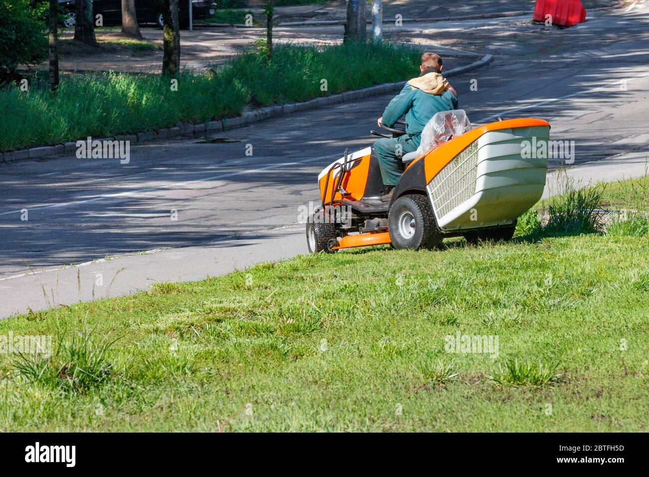 Un operatore di servizi pubblici che utilizza un rasaerba professionale taglia erba alta lungo il lato di una strada cittadina in una giornata di sole limpida, spazio per le copie. Foto Stock