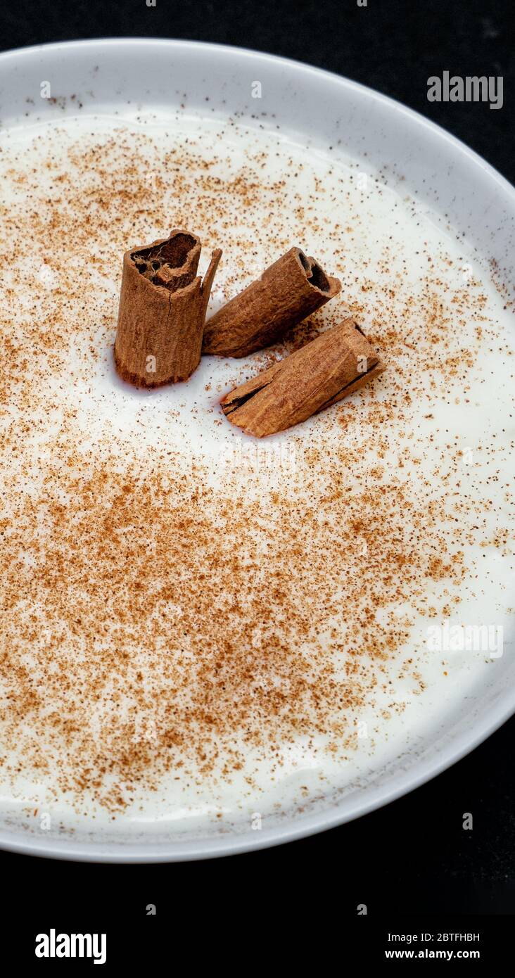 Latte di riso con cannella, piatto bianco su fondo nero Foto Stock