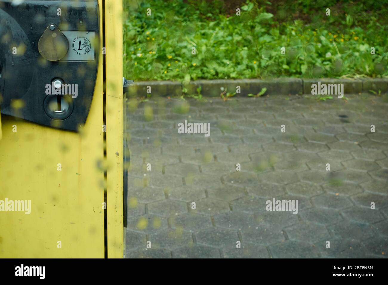 Aspirapolvere giallo, nel parcheggio, con una fessura Euro moneta, fotografato attraverso il vetro della finestra pioggia, profondità di campo, Germania. Foto Stock