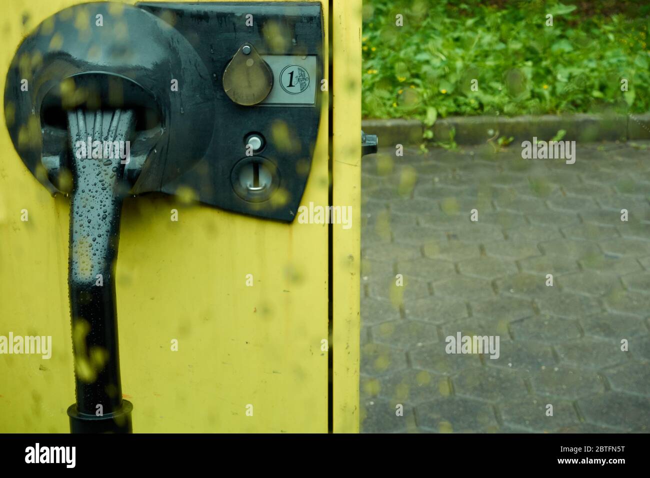 Aspirapolvere giallo, nel parcheggio, con una fessura Euro moneta, fotografato attraverso il vetro della finestra pioggia, profondità di campo, Germania. Foto Stock