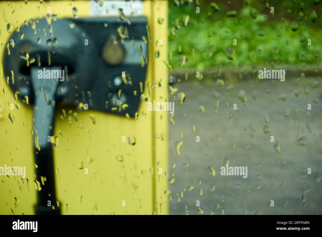 Aspirapolvere giallo, nel parcheggio, con una fessura Euro moneta, fotografato attraverso il vetro della finestra pioggia, profondità di campo, Germania. Foto Stock