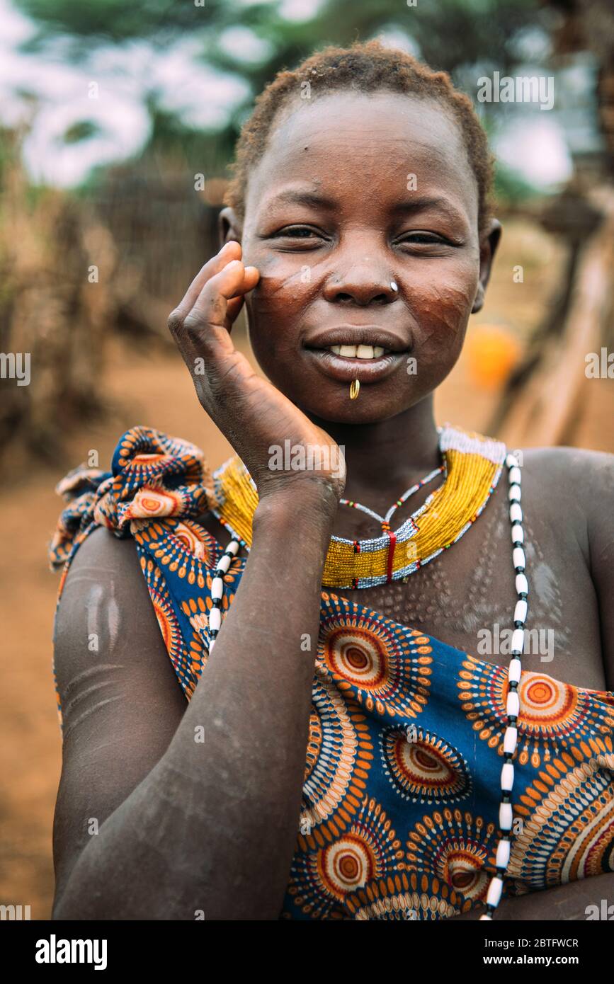 TRIBÙ TOPOSA, SUD SUDAN - 12 MARZO 2020: Giovane donna con le tradizionali cicatrici di Toposa Tribe che tocca il viso e guarda la fotocamera su sfocato Foto Stock