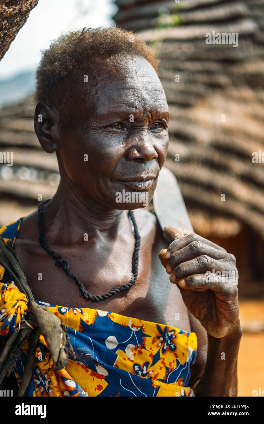 TRIBÙ BOYA, SUD SUDAN - 10 MARZO 2020: Donna anziana con capelli corti che portano il coltello sulla spalla e guardando via sullo sfondo sfocato di capanna Foto Stock