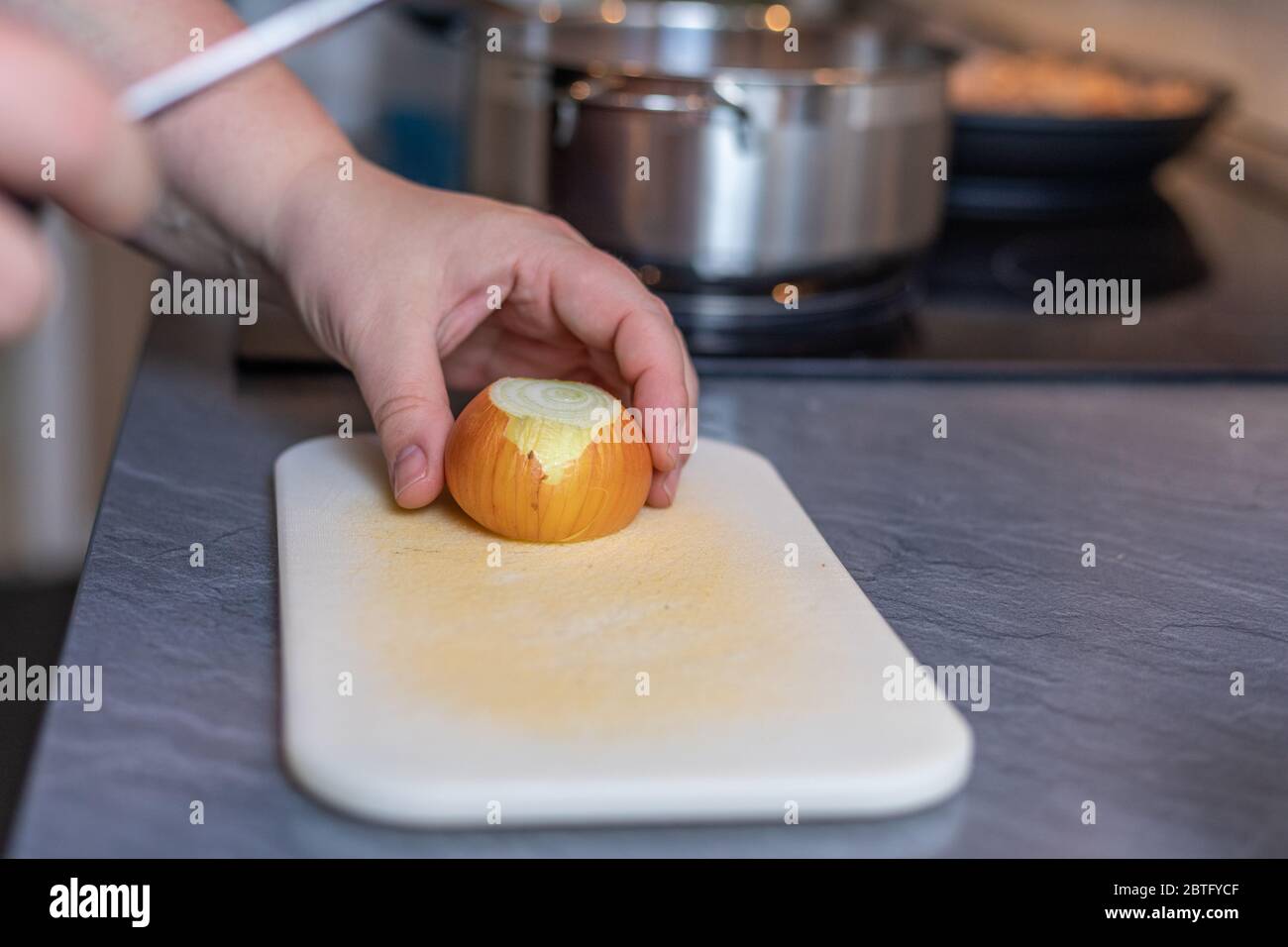 Tagliate le mani della donna il taglio di cipolla sul tagliere a tavola Foto Stock