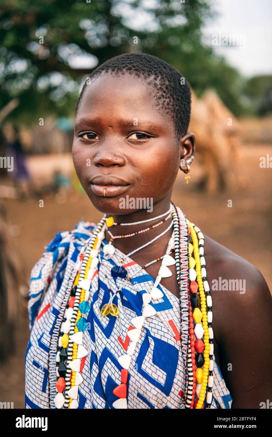 TOPOSA TRIBE, SUD SUDAN - 12 MARZO 2020: Ragazza teen in abito ornamentale e con accessori colorati guardando la fotocamera su sfondo sfocato di Foto Stock