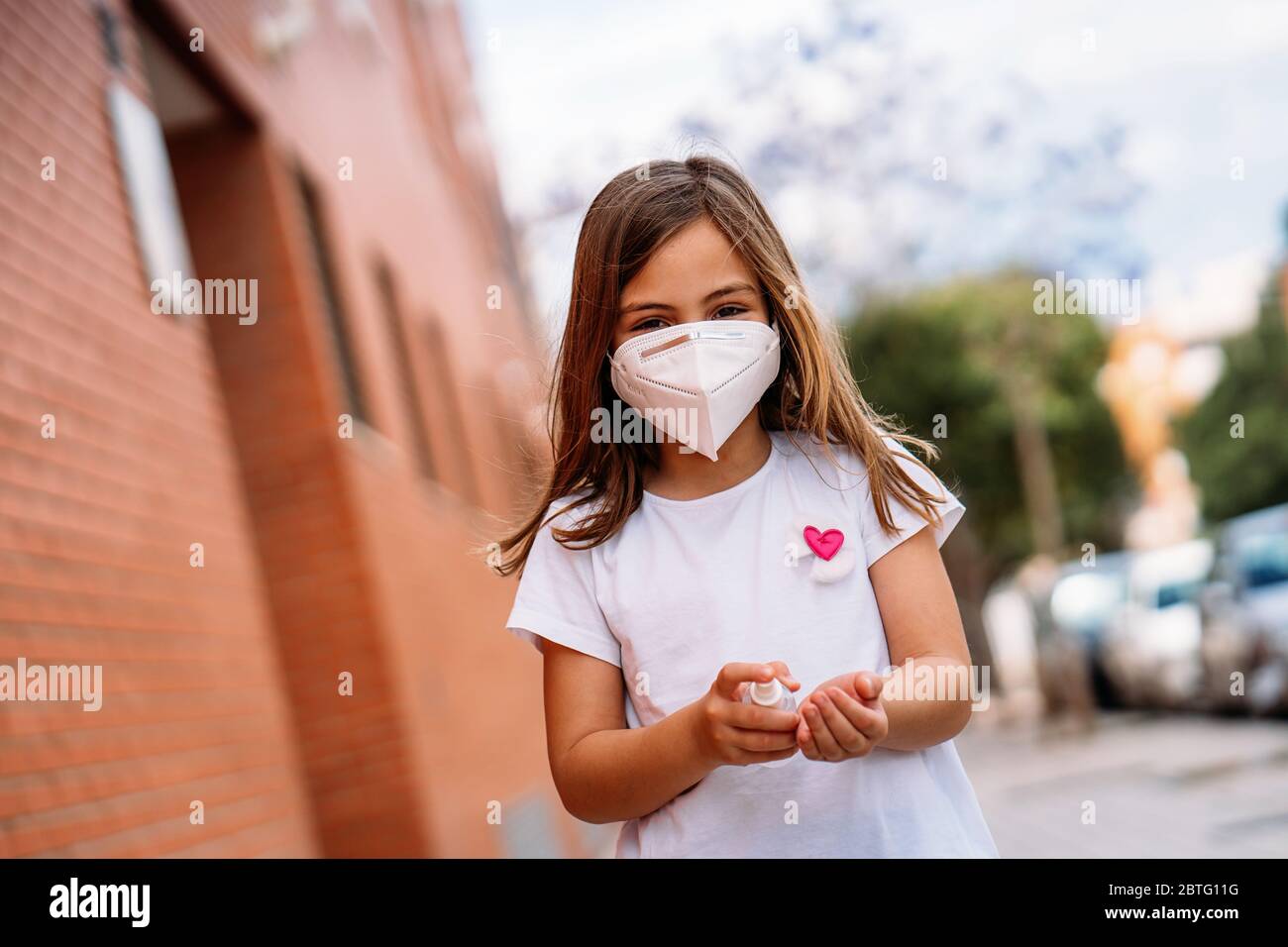 Bambina che indossa una maschera disinfettando le mani con gel idroalcolico. Foto Stock