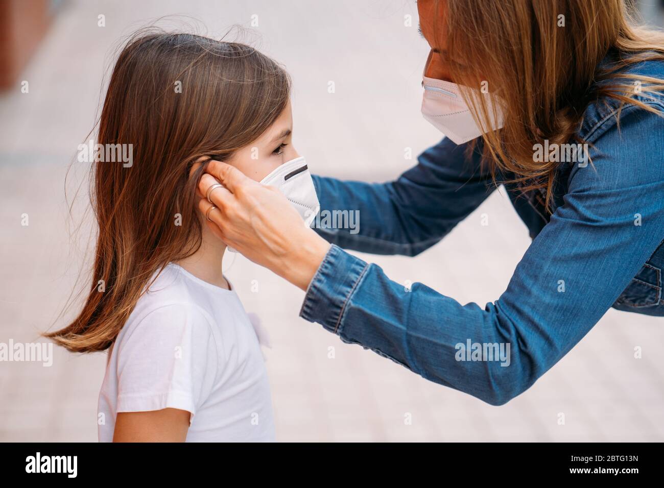 Madre che mette la maschera di faccia sulla sua figlia piccola sulla strada Foto Stock