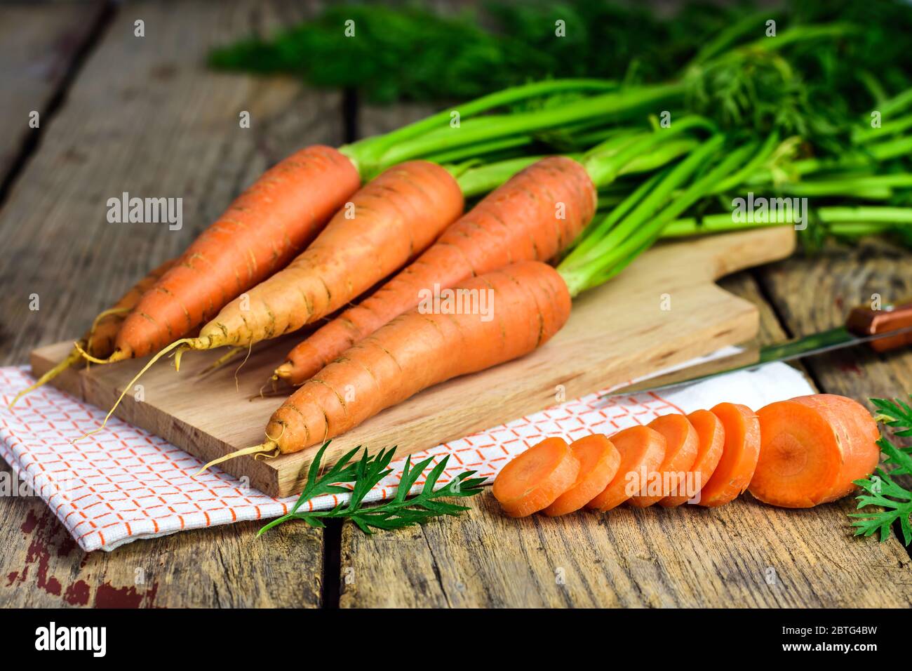 Carote fresche e carote affettate su una lavagna di legno con coltello, panno e tagliere. Messa a fuoco selettiva. Foto Stock