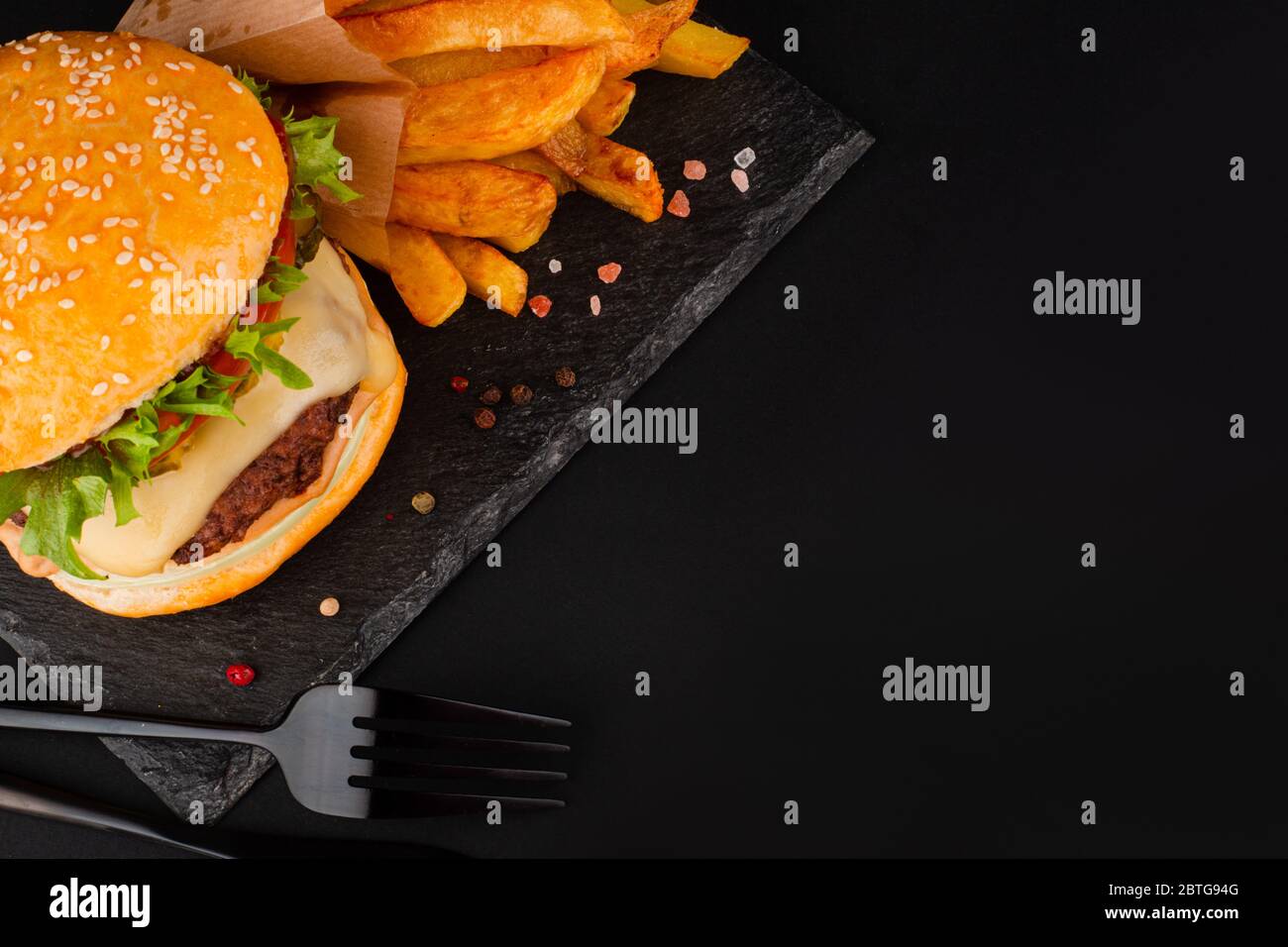 Un grande hamburger classico hamburger cheeseburger con patatine fritte su piatto di pietra nera su sfondo nero con spazio per la copia del testo Foto Stock