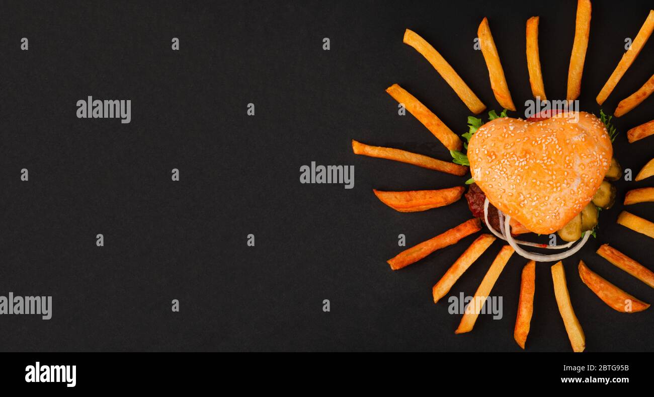 Hamburger a forma di cuore cheeseburger hamburger e patatine fritte, l'amore fast food concept, su sfondo nero, vista dall'alto piatto disposizione Foto Stock