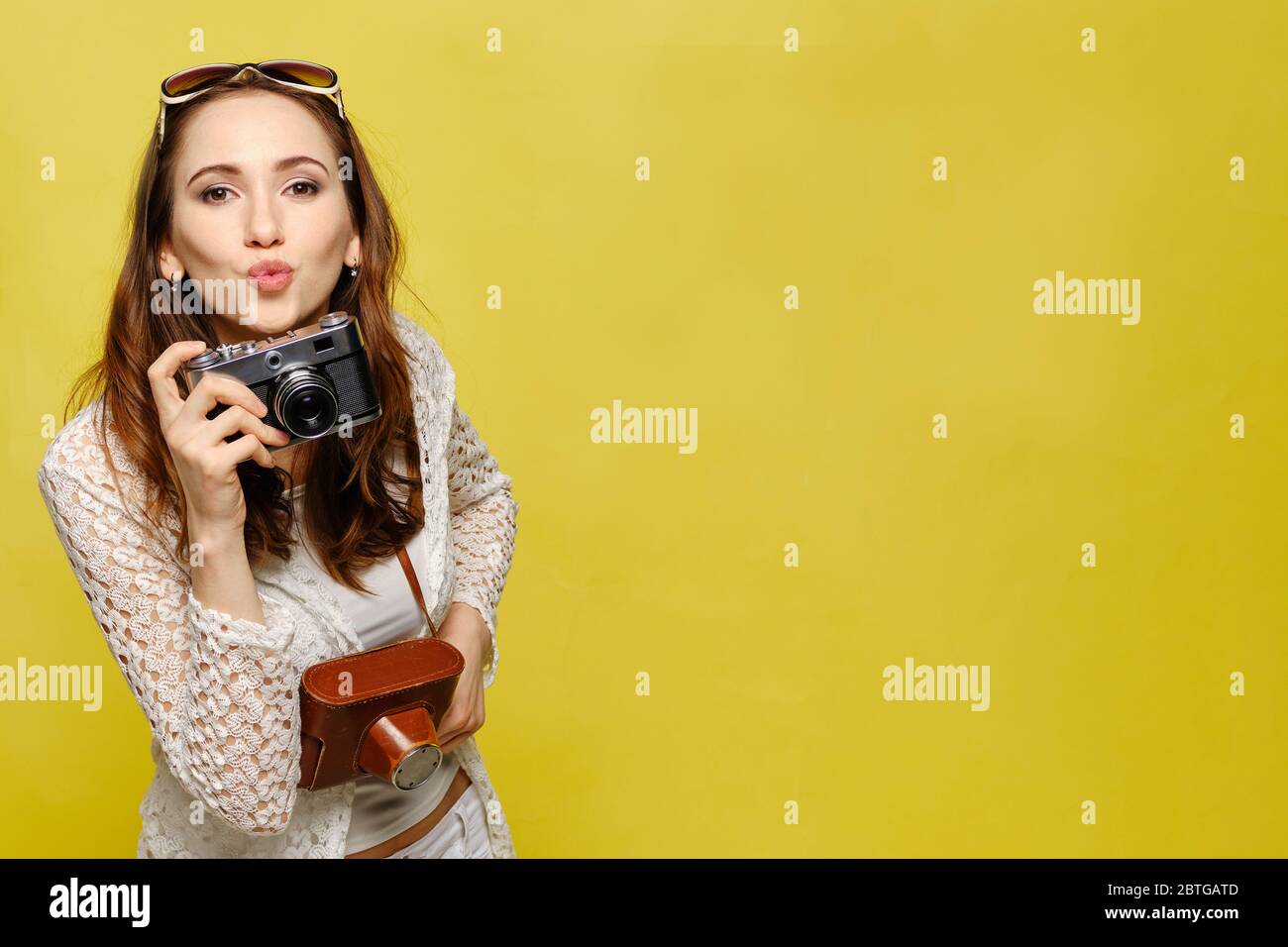 Una bella ragazza in abiti casual con una fotocamera vintage guarda la macchina fotografica e invia un bacio. Ritratto di una donna caucasica. Foto Stock