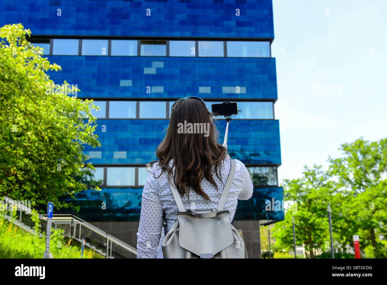 Giovane donna sorridente e che prende un selfie con il suo smartphone di fronte a un edificio di ufficio Foto Stock